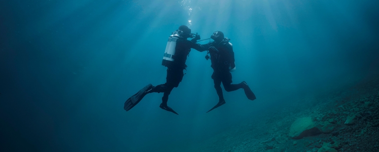 Scène sous-marine : un plongeur soutient un autre plongeur qui a des problèmes d'alimentation en air.